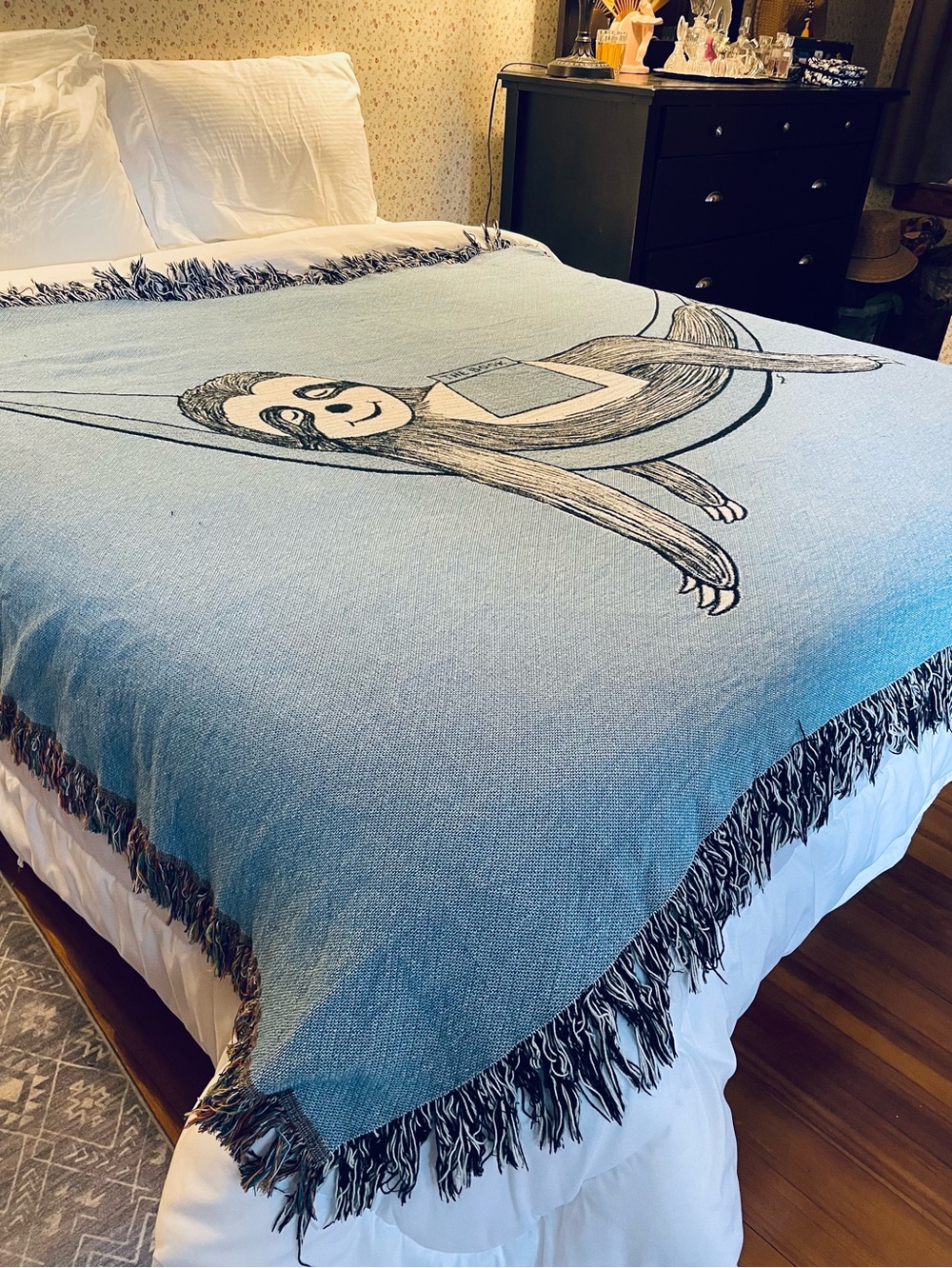 Outcasty cotton throw, relaxing sloth with book, shown on a Queen size bed